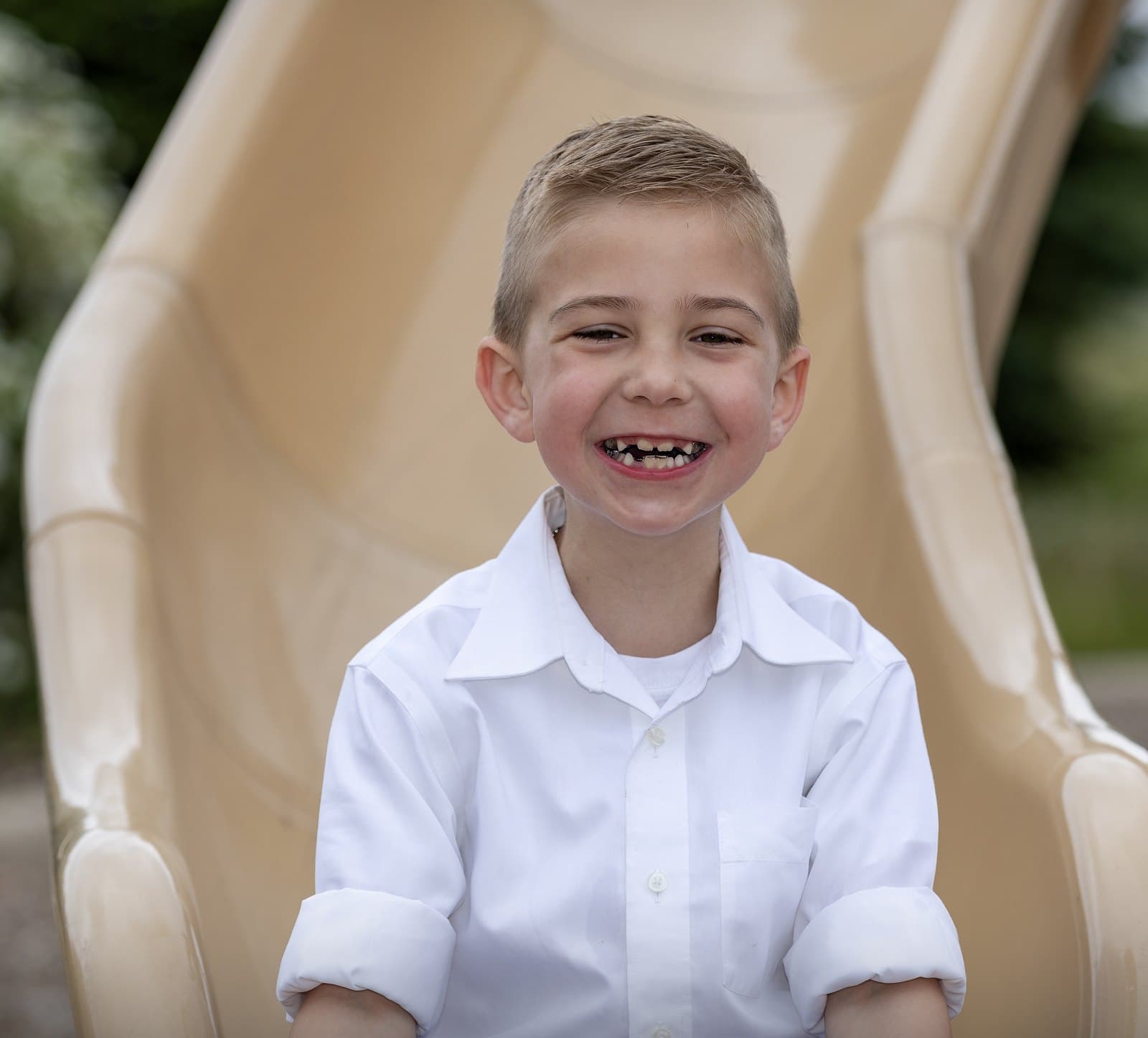 Michael around age five smiling widely at the bottom of a playground slide in a white shirt
