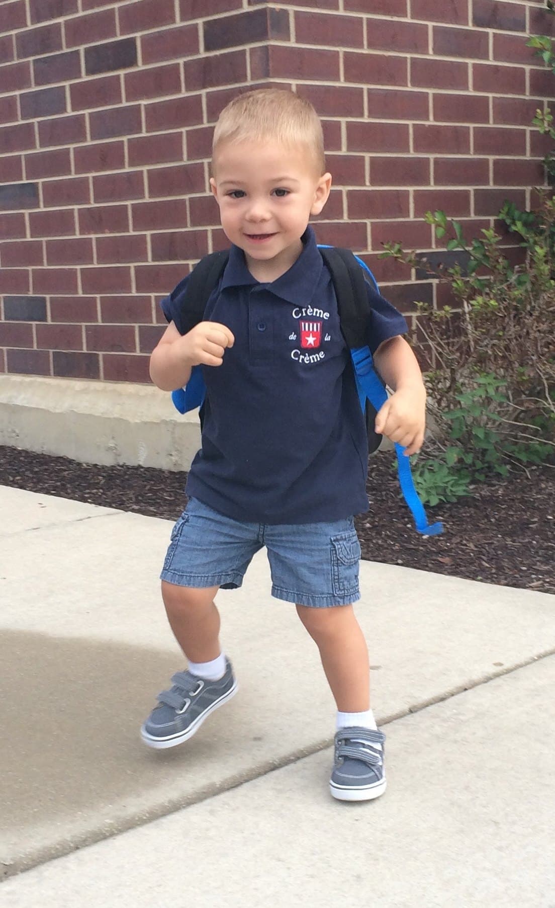 Michael at two years old walking on a sidewalk with a backpack, mouth open
